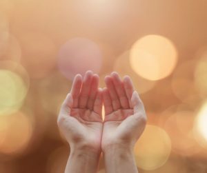 Hands clasped in prayer on candlelight background.
